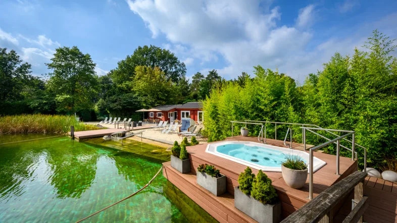 Außenwhirlpool im Aquarius Borken mit Blick auf einen ruhigen See und grüne Uferlandschaft.