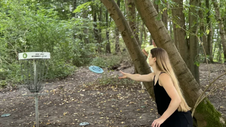 Frau wirft Frisbee beim Disc Golf im Wald in Dortmund.