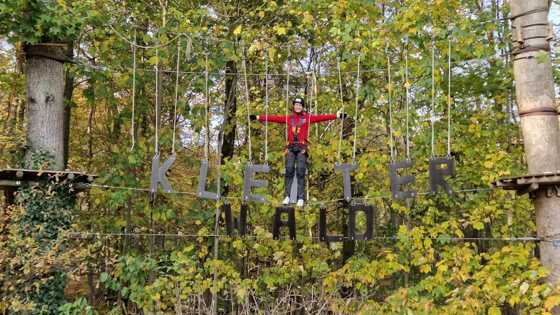 Frau auf einer schwebenden Brücke mit Bäumen im Hintergrund im Kletterwald Freischütz.