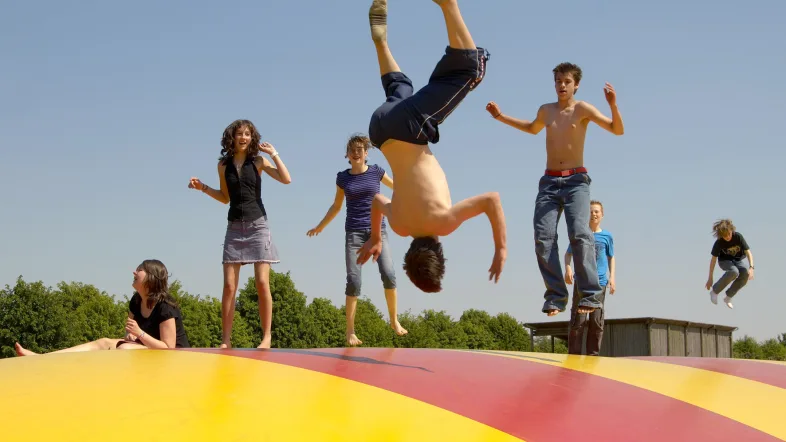 Junge macht Backflip auf bunter Hüpfburg im Archäologischen Park Xanten.