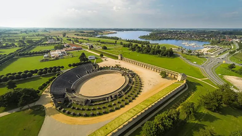 Luftaufnahme des Archäologischen Parks Xanten mit rekonstruierten römischen Bauten wie dem Amphitheater, den Thermen und dem Hafentempel, eingebettet in eine weitläufige Parklandschaft.