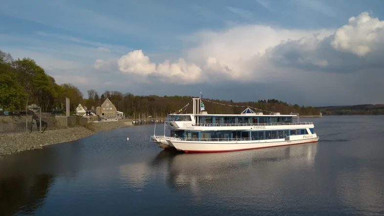 Fahrgastschiff der Möhneseeschifffahrt liegt am Ufer des Möhnesees, umgeben von Bäumen und sanften Wellen.