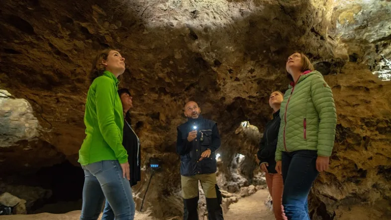 Mnschen stehen in der Kluterthöhle Ennepetal zwischen beleuchteten Felsformationen.