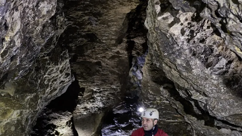 Mann sitzt in der Kluterthöhle Ennepetal auf einem Felsen zwischen Tropfsteinformationen.