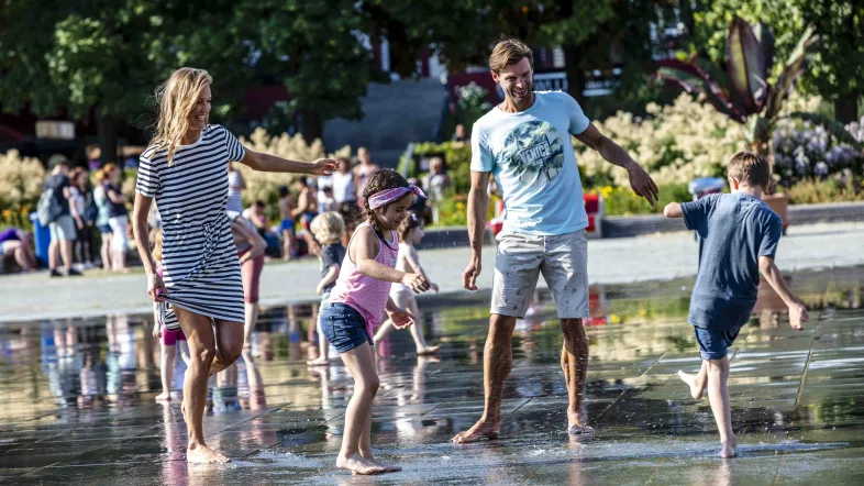 Familie genießt den Tag am Wasserspielbereich im Sauerlandpark Hemer mit spielenden Kindern im Hintergrund.