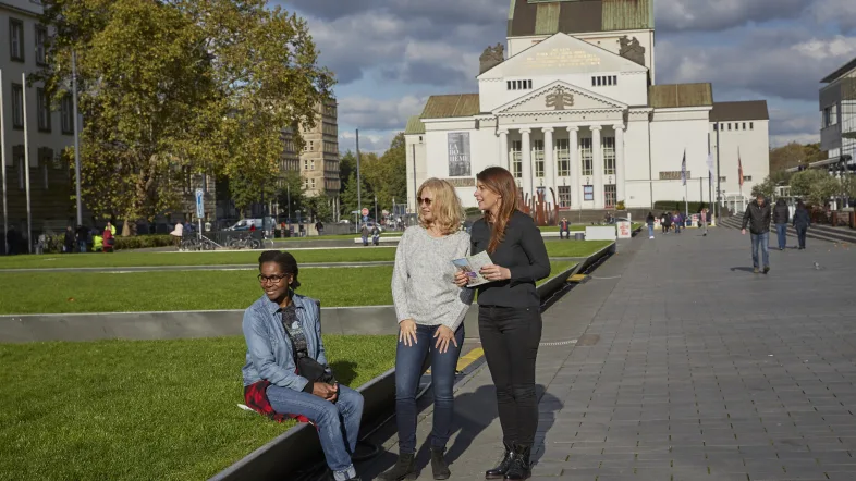 Drei Frauen nehmen an einer Stadtführung in Duisburg teil und hören aufmerksam dem Guide zu.