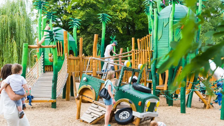 Kinder spielen auf dem naturnah gestalteten Spielplatz im Tierpark Bochum bei sonnigem Wetter.
