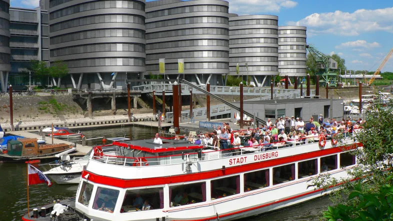 Ausflugsschiff der Weißen Flotte Duisburg im Innenhafen, umgeben von modernen Gebäuden und Wasser.