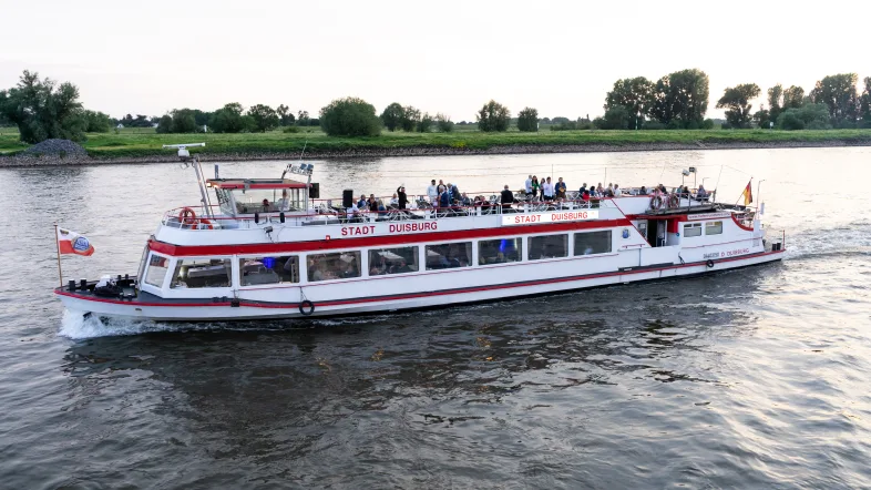 Luftaufnahme der Weißen Flotte Duisburg mit einem Schiff auf dem Wasser und umliegender Stadt.