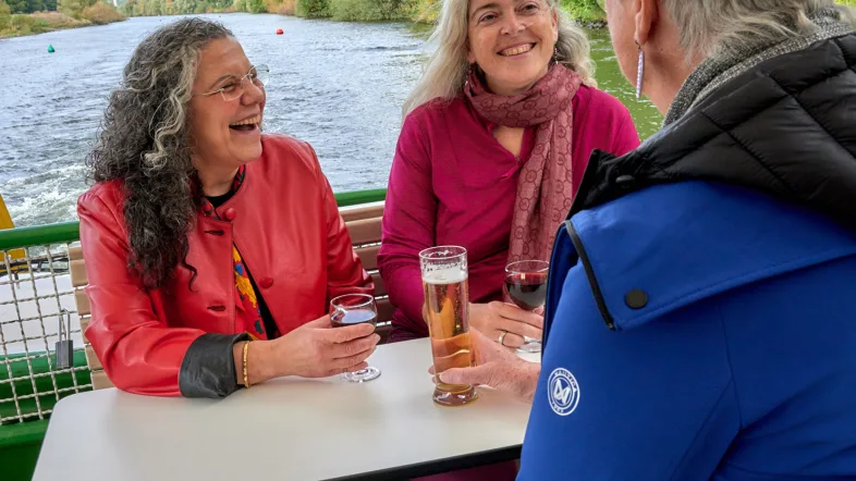 Gäste an Bord der „Weißen Flotte“ Mülheim genießen Getränke und die Aussicht auf dem Fluss.